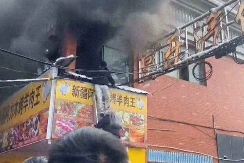 浓浓黑烟把二楼店铺吞没,一名受困人员顺着梯子从阳台逃生。(路透社)